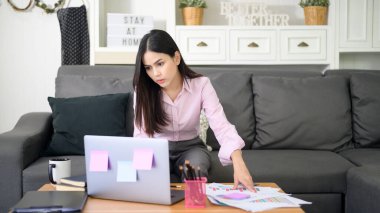 Bir iş kadını dizüstü bilgisayarla çalışıyor ve oturma odasında iş geliştirme grafik verilerini analiz ediyor, evden çalışıyor, iş teknolojisi kavramını inceliyor . 