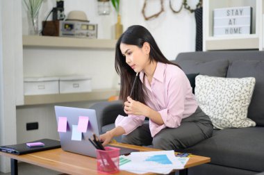 Bir iş kadını dizüstü bilgisayarla çalışıyor ve oturma odasında iş geliştirme grafik verilerini analiz ediyor, evden çalışıyor, iş teknolojisi kavramını inceliyor . 