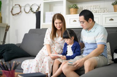 Mutlu Asyalı ebeveyn küçük tatlı kızına ev ödevi yapmayı öğretiyor ve evde resim çiziyor.. 