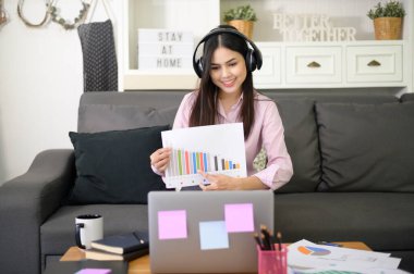 Kulaklık takan genç ve güzel bir kadın evdeki bilgisayarla video konferans görüşmesi yapıyor, iş teknolojisi kavramı. . 