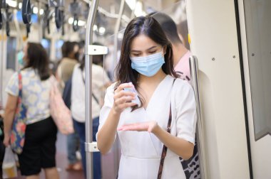 Metroda koruyucu maske takan genç bir kadın el yıkamak için alkol kullanıyor, Covid-19 salgını, güvenlik seyahati, sosyal mesafe protokolü, yeni normal seyahat kavramı altında seyahat ediyor.