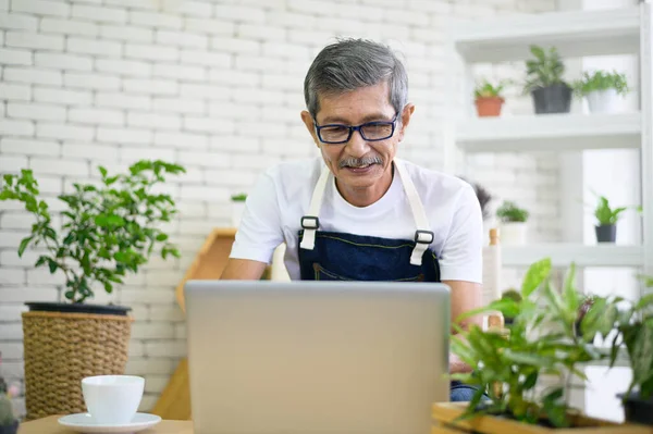 Dizüstü bilgisayarlı yaşlı Asyalı emekli adam evinde dinleniyor ve eğleniyor..