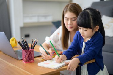 Asyalı Mutlu anne ve kızı evde internet üzerinden çalışmak için dizüstü bilgisayar kullanıyorlar. Karantina zamanında e-öğrenim kavramı