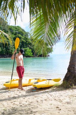 Güneşli bir günde okyanusta kano süren genç bir sporcu.