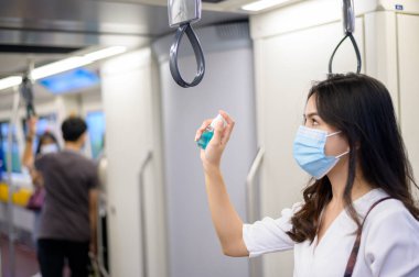 Metroda koruyucu maske takan genç bir kadın el yıkamak için alkol kullanıyor, Covid-19 salgını, güvenlik seyahati, sosyal mesafe protokolü, yeni normal seyahat kavramı altında seyahat ediyor.