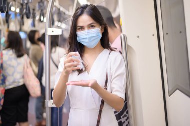 Metroda koruyucu maske takan genç bir kadın el yıkamak için alkol kullanıyor, Covid-19 salgını, güvenlik seyahati, sosyal mesafe protokolü, yeni normal seyahat kavramı altında seyahat ediyor.