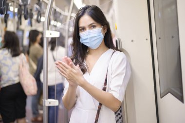 Metroda koruyucu maske takan genç bir kadın el yıkamak için alkol kullanıyor, Covid-19 salgını, güvenlik seyahati, sosyal mesafe protokolü, yeni normal seyahat kavramı altında seyahat ediyor.
