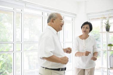 Neşeli yaşlı Asyalı emekli çift evdeki oturma odasında dans ediyor ve müziğin tadını çıkarıyor. Sağlık konsepti.