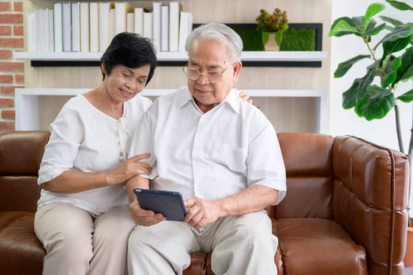 A happy senior Asian couple is using tablet and talking with family on webcam at home, retirement concept.