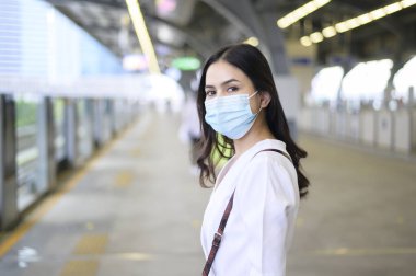 Genç bir kadın metro istasyonunda duruyor, maske takıyor, Covid-19 koruma, yeni normal seyahat konsepti.