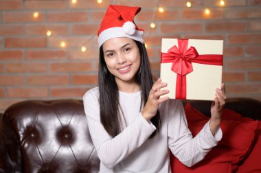 Kırmızı Noel Baba şapkası takan genç bir kadın Noel günü hediye kutusunu gösteriyor, tatil konsepti..