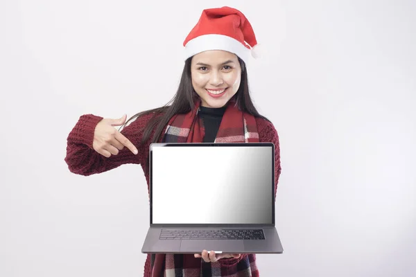 Young smiling woman wearing red Santa Claus hat making with laptop screen mock up  on white