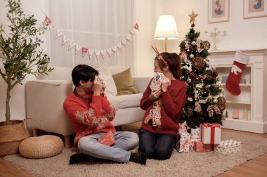 Şenlikli çift, Noel neşesiyle dolu dekore edilmiş bir oturma odasında hediyelerini paylaşmayı sever..
