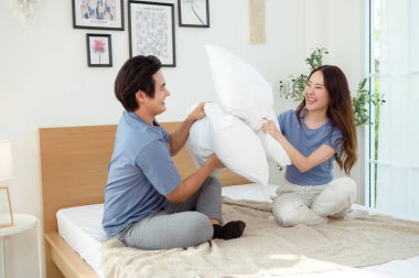 Bir çift yastık kavgasından zevk alıyor, yatakta birlikte gülüyorlar..