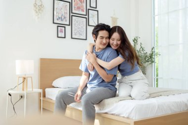 Işıl ışıl bir yatak odasında bir yatakta otururken iki insan sıcak bir kucaklaşmayı paylaşıyor..