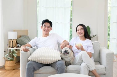 Neşeli bir çift kanepede birlikte oturur, güneşli bir yerde tatlı köpekleri ile atıştırmalıkları paylaşır..