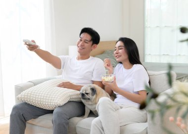 Neşeli bir çift kanepede birlikte oturur, güneşli bir yerde tatlı köpekleri ile atıştırmalıkları paylaşır..