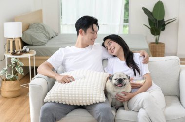 Neşeli bir çift kanepede birlikte oturur, güneşli bir yerde tatlı köpekleri ile atıştırmalıkları paylaşır..