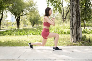 Bir kadın parkta asfalt bir yolda hamle yaparak egzersiz yapıyor..