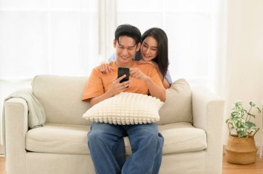 Bir çift, bir kanepede oturup, akıllı telefona bakarken neşe anlarını paylaşıyor..