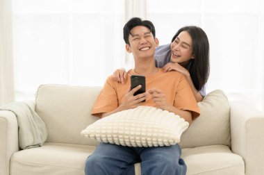 Bir çift, bir kanepede oturup, akıllı telefona bakarken neşe anlarını paylaşıyor..