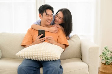 Bir çift, bir kanepede oturup, akıllı telefona bakarken neşe anlarını paylaşıyor..