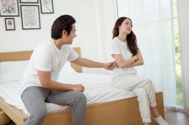 Bir çift, modern odalarında bir yatakta oturup, gerginlik ve üzüntü ifade ederler..