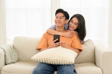 Bir çift, bir kanepede oturup, akıllı telefona bakarken neşe anlarını paylaşıyor..