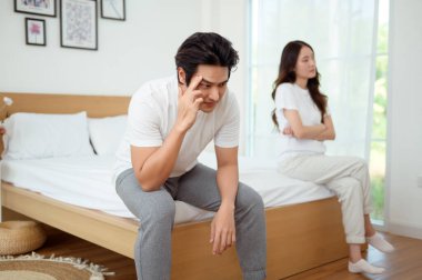 Bir çift, modern odalarında bir yatakta oturup, gerginlik ve üzüntü ifade ederler..