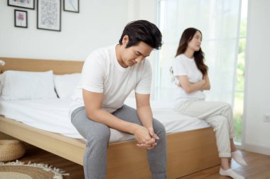 Bir çift, modern odalarında bir yatakta oturup, gerginlik ve üzüntü ifade ederler..