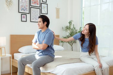 Bir çift, modern odalarında bir yatakta oturup, gerginlik ve üzüntü ifade ederler..