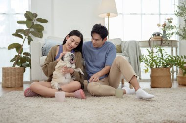 Köpekleri ile oynarlarken gülümseyen bir çift güzel ışıklandırılmış bir oturma odasında yumuşak bir halıda.