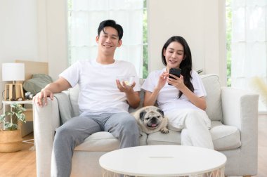 Neşeli bir çift kanepede birlikte oturur, güneşli bir yerde tatlı köpekleri ile atıştırmalıkları paylaşır..