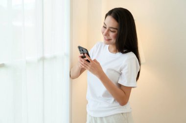 Bir kadın akıllı telefonuyla meşgul, aydınlık bir odada gülümsüyor..