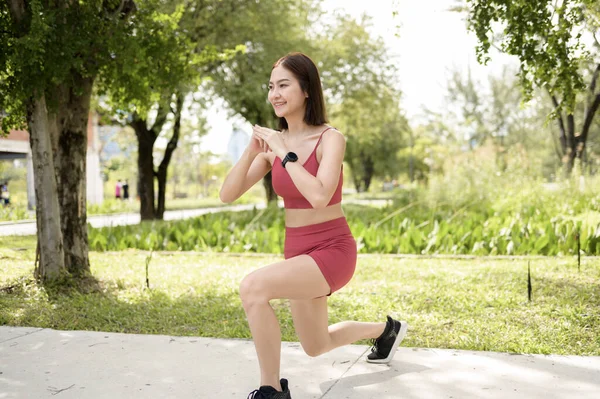 Bir kadın parkta asfalt bir yolda hamle yaparak egzersiz yapıyor..