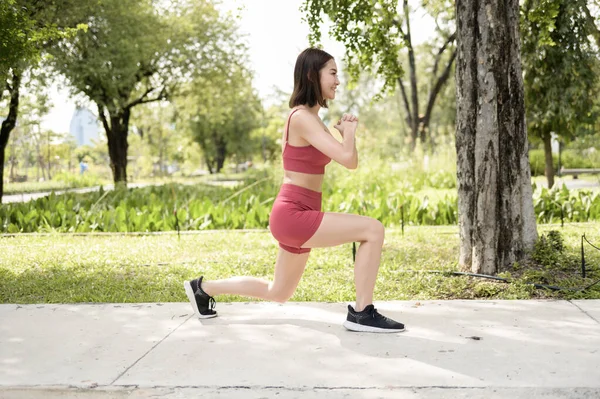 Bir kadın parkta asfalt bir yolda hamle yaparak egzersiz yapıyor..