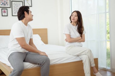 Bir çift, modern odalarında bir yatakta oturup, gerginlik ve üzüntü ifade ederler..