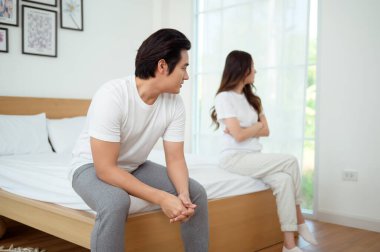 Bir çift, modern odalarında bir yatakta oturup, gerginlik ve üzüntü ifade ederler..