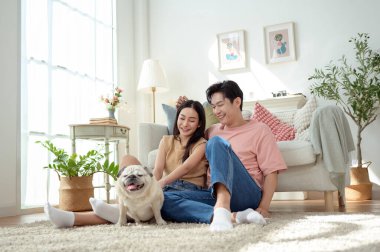 Köpekleri ile oynarlarken gülümseyen bir çift güzel ışıklandırılmış bir oturma odasında yumuşak bir halıda.