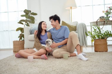 Köpekleri ile oynarlarken gülümseyen bir çift güzel ışıklandırılmış bir oturma odasında yumuşak bir halıda.