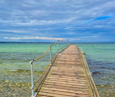 Güzel bulutlu gökyüzü ile sakin okyanus sularına uzanan ahşap bir iskele manzarası..