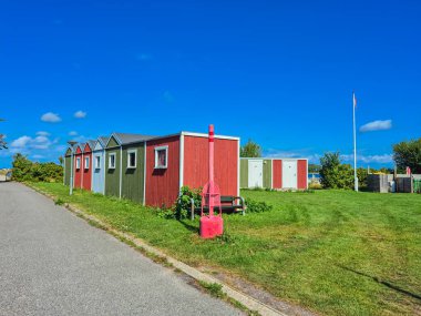 Çok renkli kulübeler, canlı yeşil otların eşlik ettiği manzaralı bir yol kenarında güzel bir şekilde sıralanmıştır.