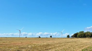 Rüzgâr türbinleri, sürdürülebilir enerjiye ve temiz bir çevreye önemli ölçüde katkıda bulunan geniş bir açık alanda dimdik dururlar.