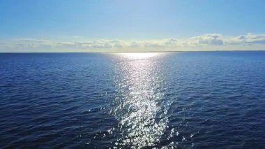 Huzurlu ve sakin bir okyanus manzarası, suda parıldayan güneş ışığının güzel ve çarpıcı yansımaları.