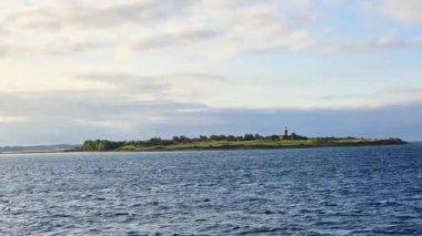 Büyüleyici bir adada sakin sularda tarihi bir deniz feneri ve açık, parlak bir gökyüzü bulunur.