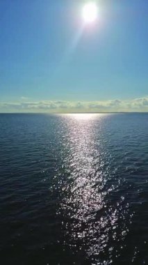 Huzurlu bir okyanus manzarası sakin ve huzurlu sulardan yansıyan parlak güneş ışığını sergiliyor.