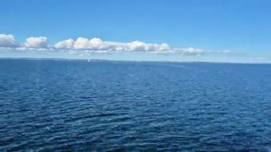 Sakin okyanusun nefes kesen manzarası, berrak mavi gökyüzünü kabarık bulutların yanında güzel yansıtıyor.