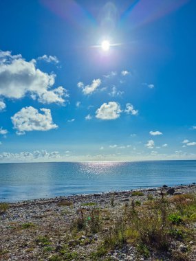 Parlak bir güneş ve kabarık bulutların altında parıldayan, ışıldayan, ışıl ışıl parlayan bir deniz manzarası.