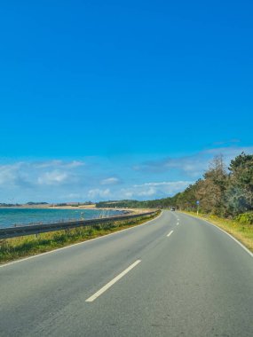 Güzel, sakin bir kıyı manzarasının yanında uzanan dolambaçlı bir yolu gösteren nefes kesici bir manzara.