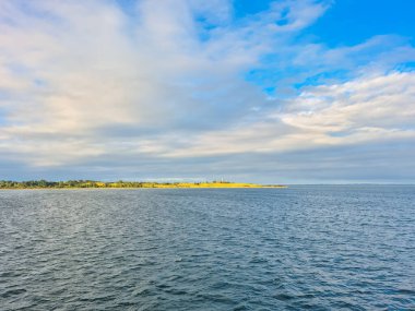 Sakin suların ve geniş mavi gökyüzünün altında yemyeşil kıyı şeritlerinin yer aldığı sakin ve sakin bir manzara.